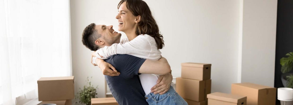 Eerste woning een droom die uitkomt jongen tilt een vrouw op in een woonkamer met allemaal dozen