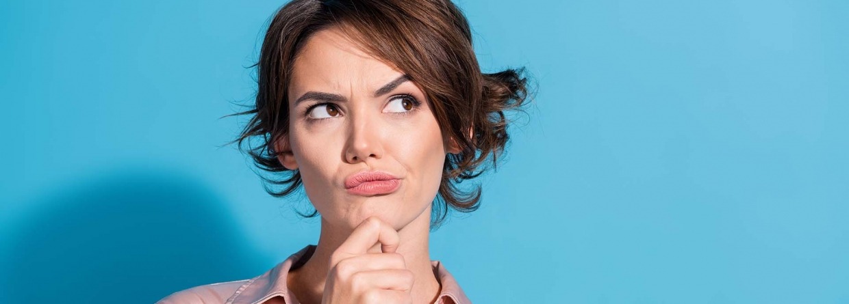 Denkende vrouw met haar hand op haar kin draagt een roze satijnen blouse en stata voor een blauwe achtergrond