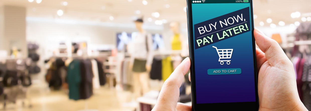 BNPL Buy Now Pay Later online shopping; hand met mobiele telefoon en op de achtergrond een winkel