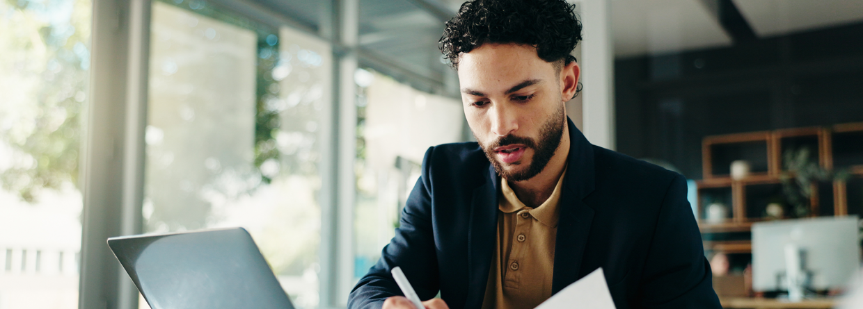 Man achter een bureau met laptop voor zich en een pen en document in zijn is een controle aan het uitvoeren