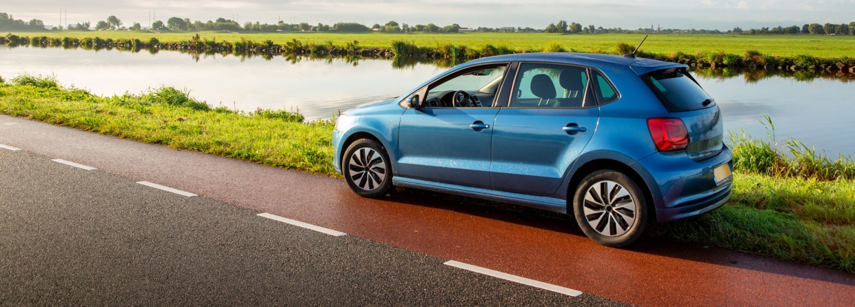Een blauwe auto staat geparkeerd langs de kant van de weg op een bewolkte dag in Nederland.