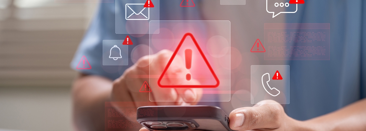 Man achter laptop met telefoon in de hand waarop allerlei phising meldingen gegeven worden