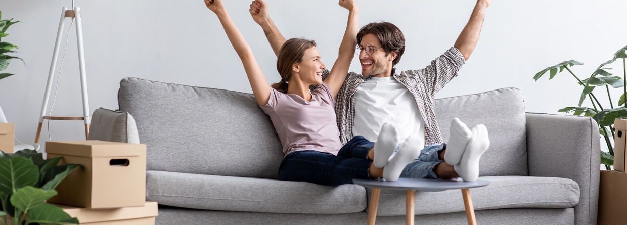 Jong stel dat samen is gaan wonen en op de bank zit met de armen omhoog van blijdschap