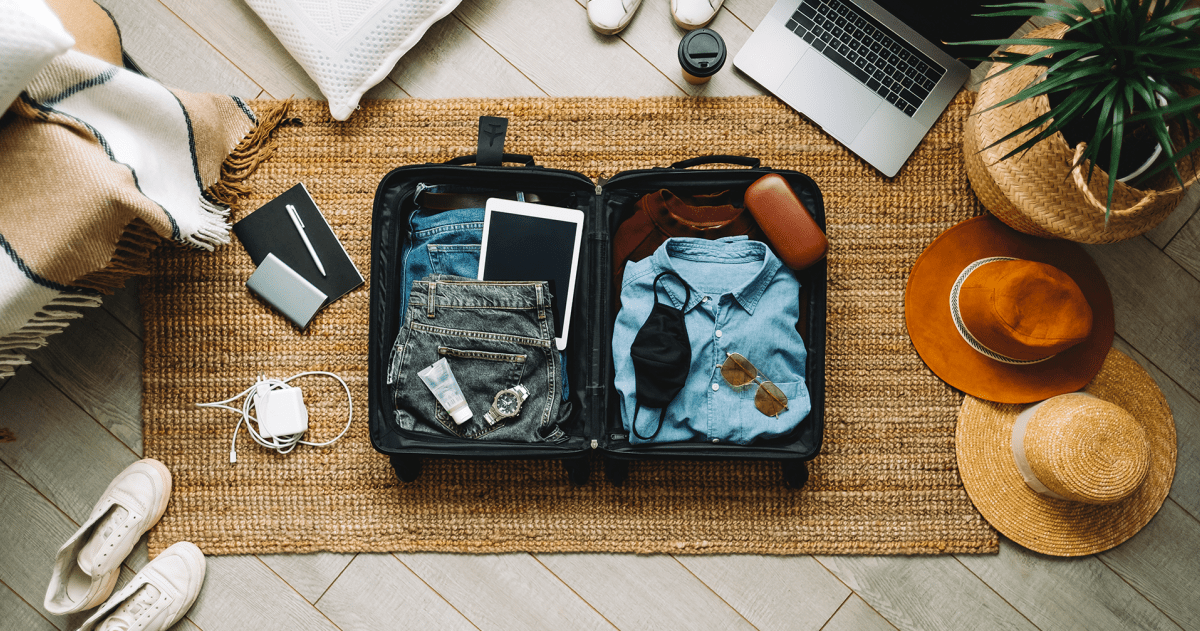 Campagne vakantiegevoel; koffer met kleding, schoenen, hoeden en digitale apparatuur uitgestald op de grond