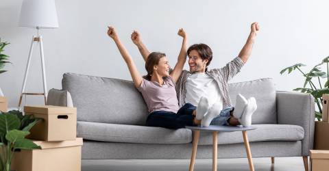 Jong stel dat samen is gaan wonen en op de bank zit met de armen omhoog van blijdschap